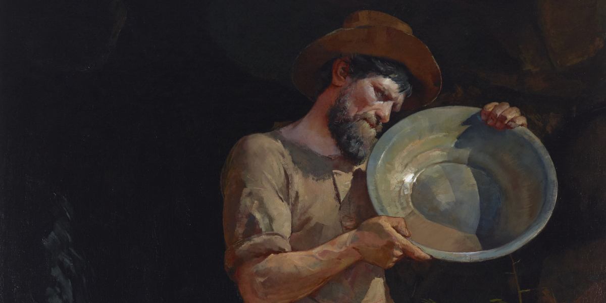 A prospector holding and looking at a pan