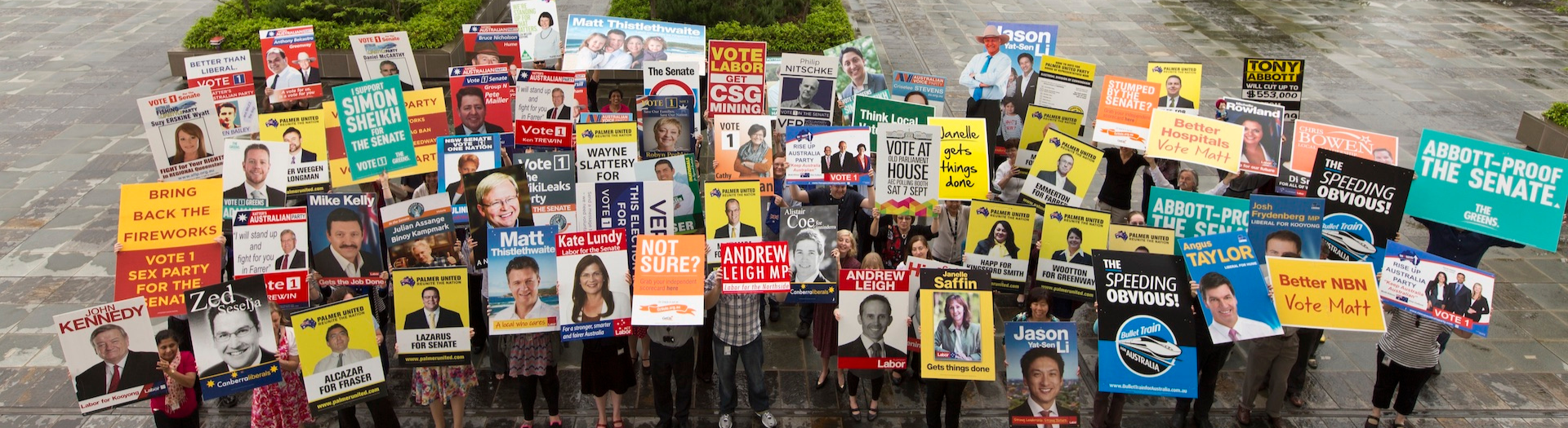 People standing holding colourful core-flutes/posters from the 2013 election