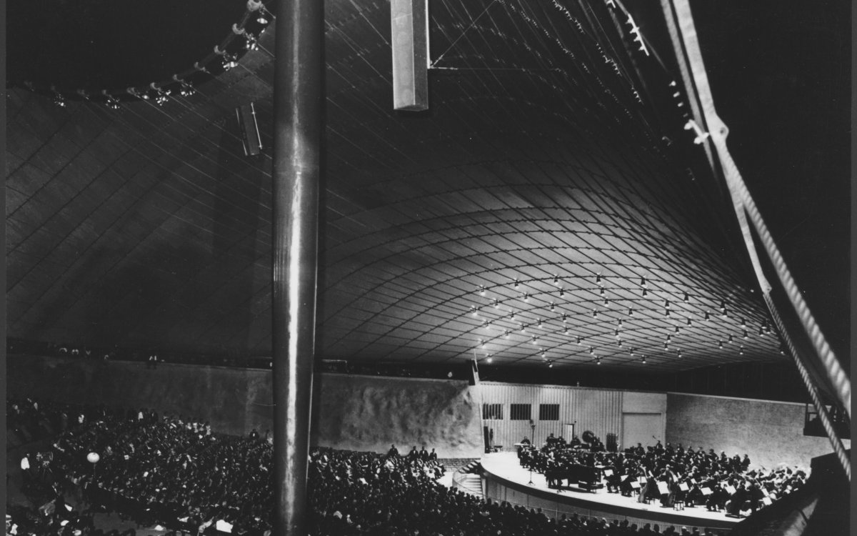 A black and white photograph of the Sidney Myer Music Bowl. A large crowd is watching a performance of an orchestra on the stage.