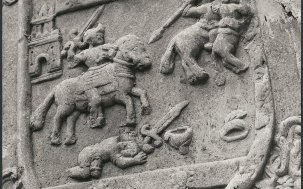 A close up of an architectural detail on a building. The detail is a knight on horseback fighting. The image is enclosed in a shield.