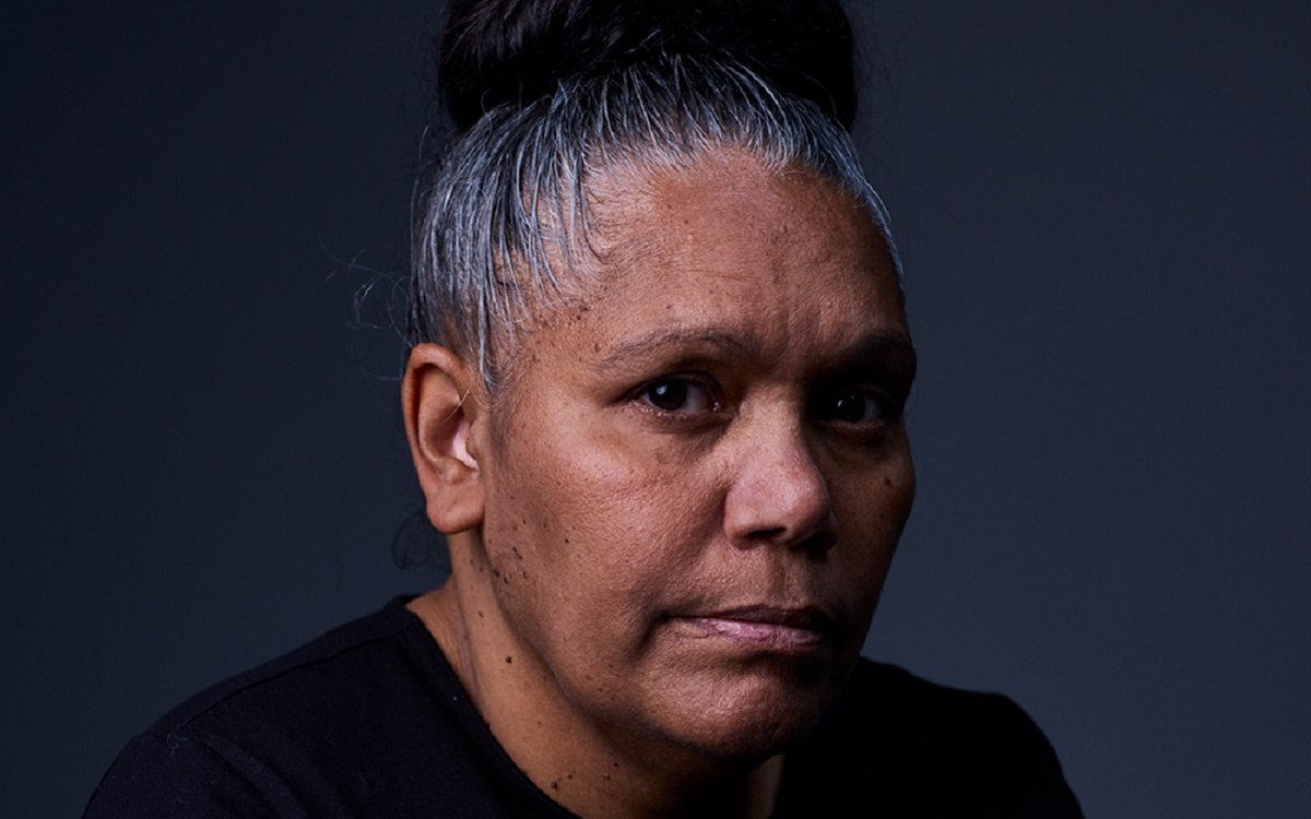 A headshot of an Aboriginal woman. She has her hair ties up in a bun and is wearing a black shirt.