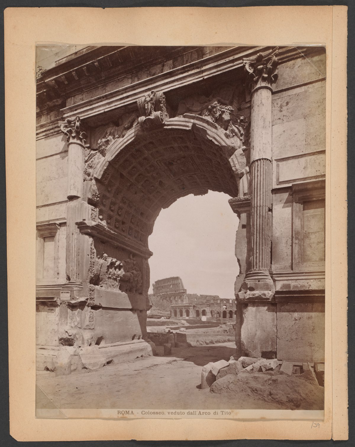 A sepia toned photograph showing the ruins of the Colosseum viewed through the ruins of the Arch of Titus. At the bottom of the photo are words in Italian: "ROMA - Colosseo, verduto dali Arco di Tito" 