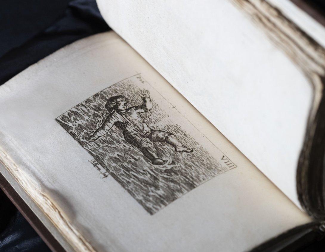 A rare book about swimming held open. Left side is a black and white illustration of a person floating on the surface of water. 