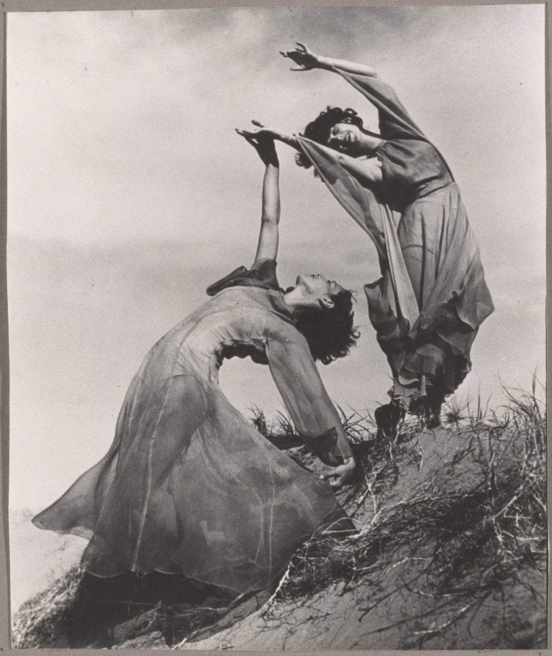 A black and white photograph of two women in long dresses posing on a sand bank