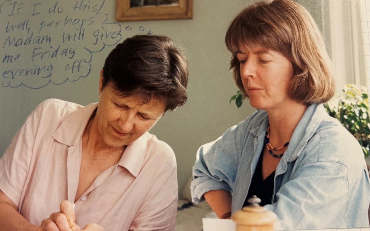 Two women looking down at something out of frame. One is wearing a pink shirt and one is wearing a blue shirt.