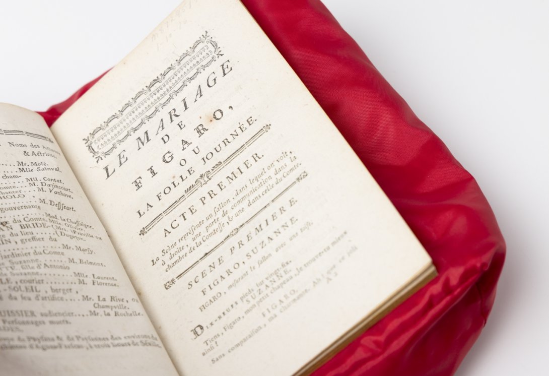 Open printed book on a red cushion, open to the opening act of the play The Marriage of Figaro in French