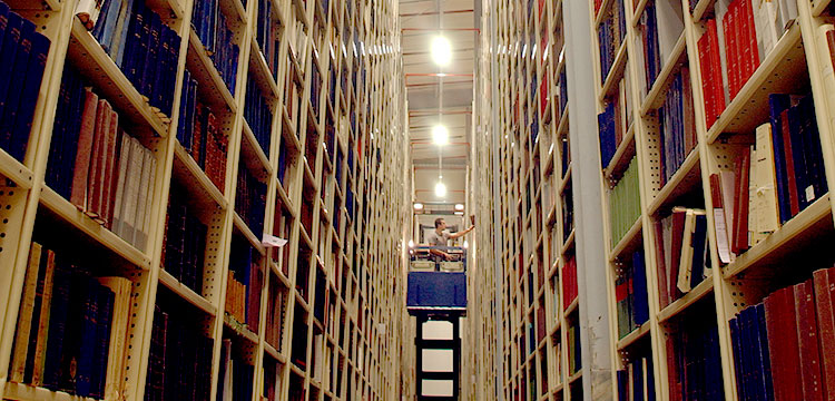 A person using a lift to reach books in the library storage stacks