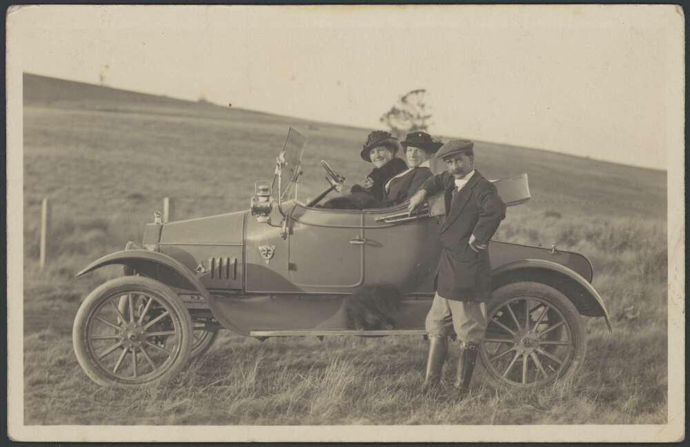 Three people posing in an old motor car