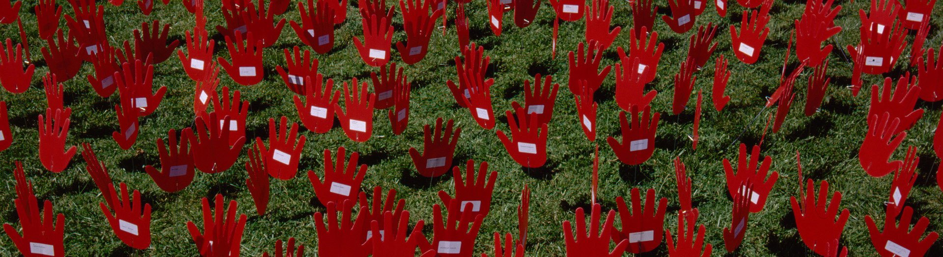 A photo full of red plastic hads with white name tags stuck on the palms, attached to a long wire planted in green ground cover foliage.