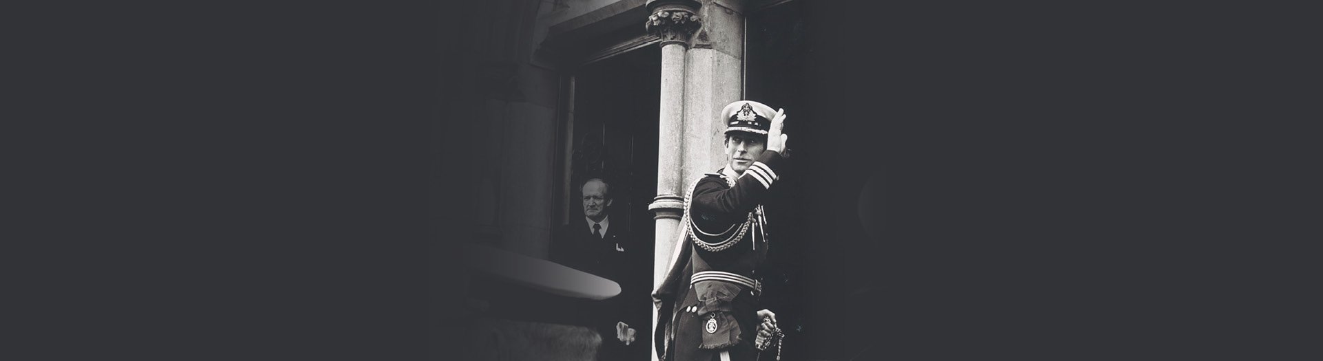 A black banner with a black and white image of a man in uniform waving in front of a house.