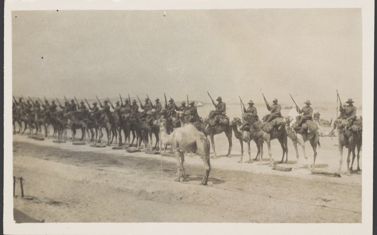 Sepia photograph of World War One soldiers mounted on camels lined up for inspection on the sand