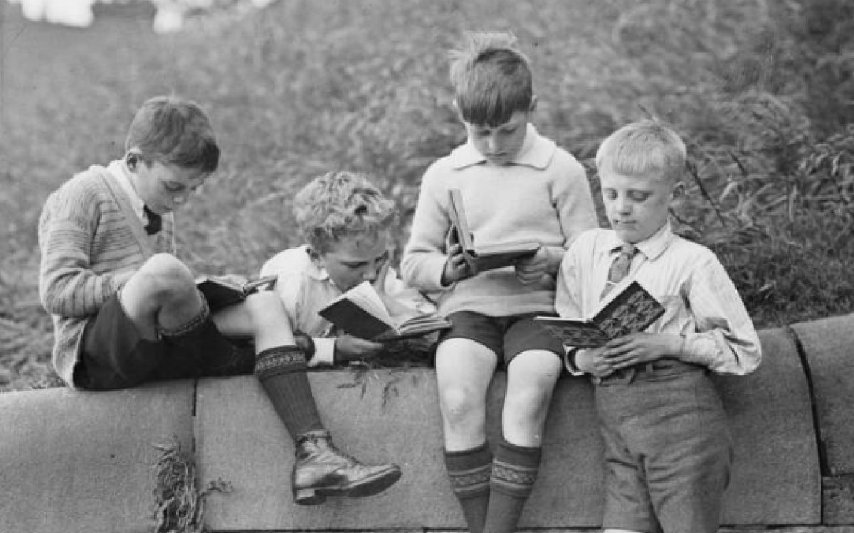 Four boys sitting on a wall reading books