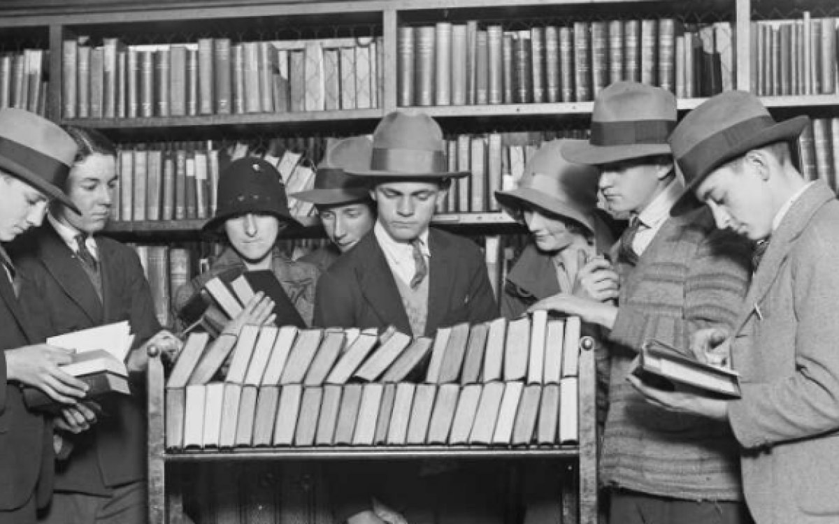 Nine people gathered around trolley of books in a library