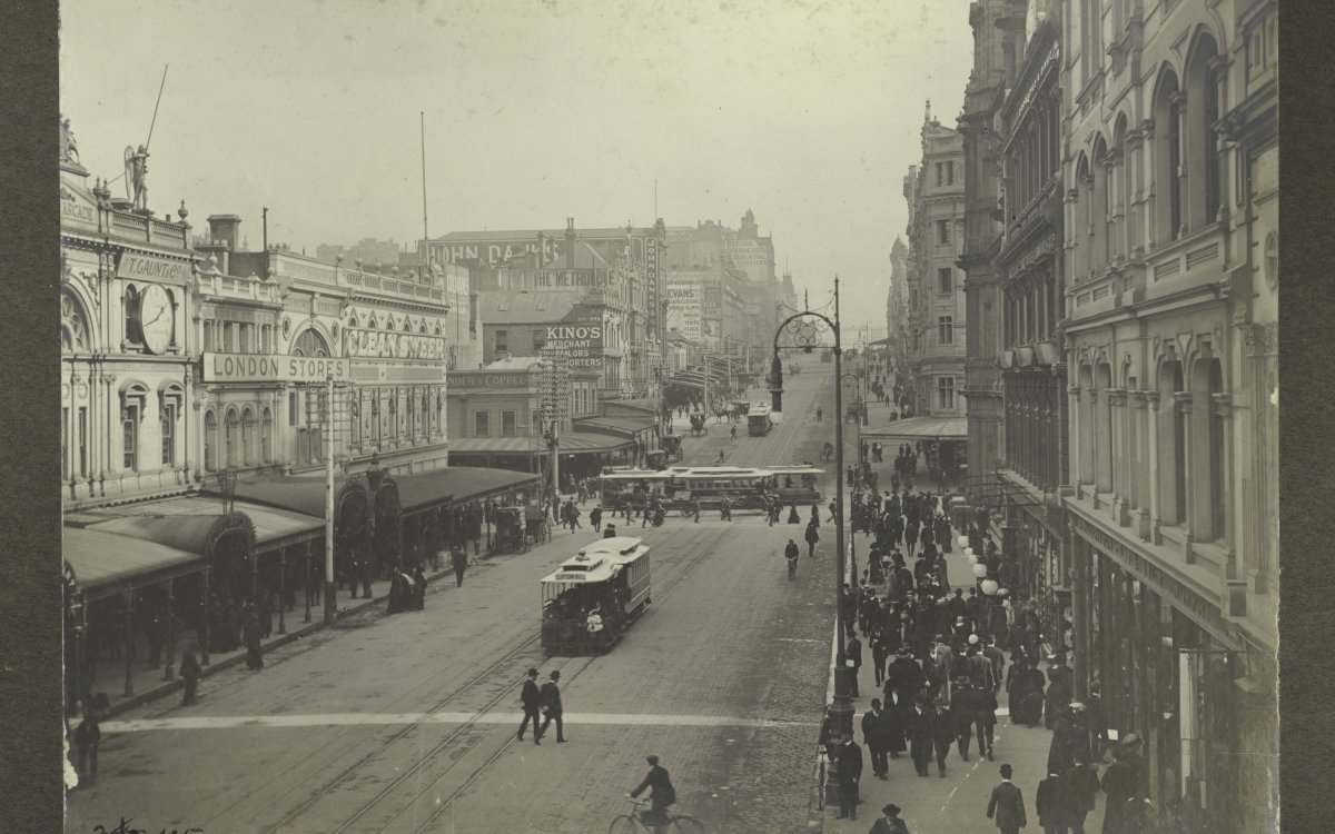 Photograph showing Bourke Street, Melbourne in the early 1900s. People crowd the footpath while two trams run along the street. Shop signs in view: "T. Gaunt and co.", "London stores", Kino's merchant", "John Danks and so[n]".