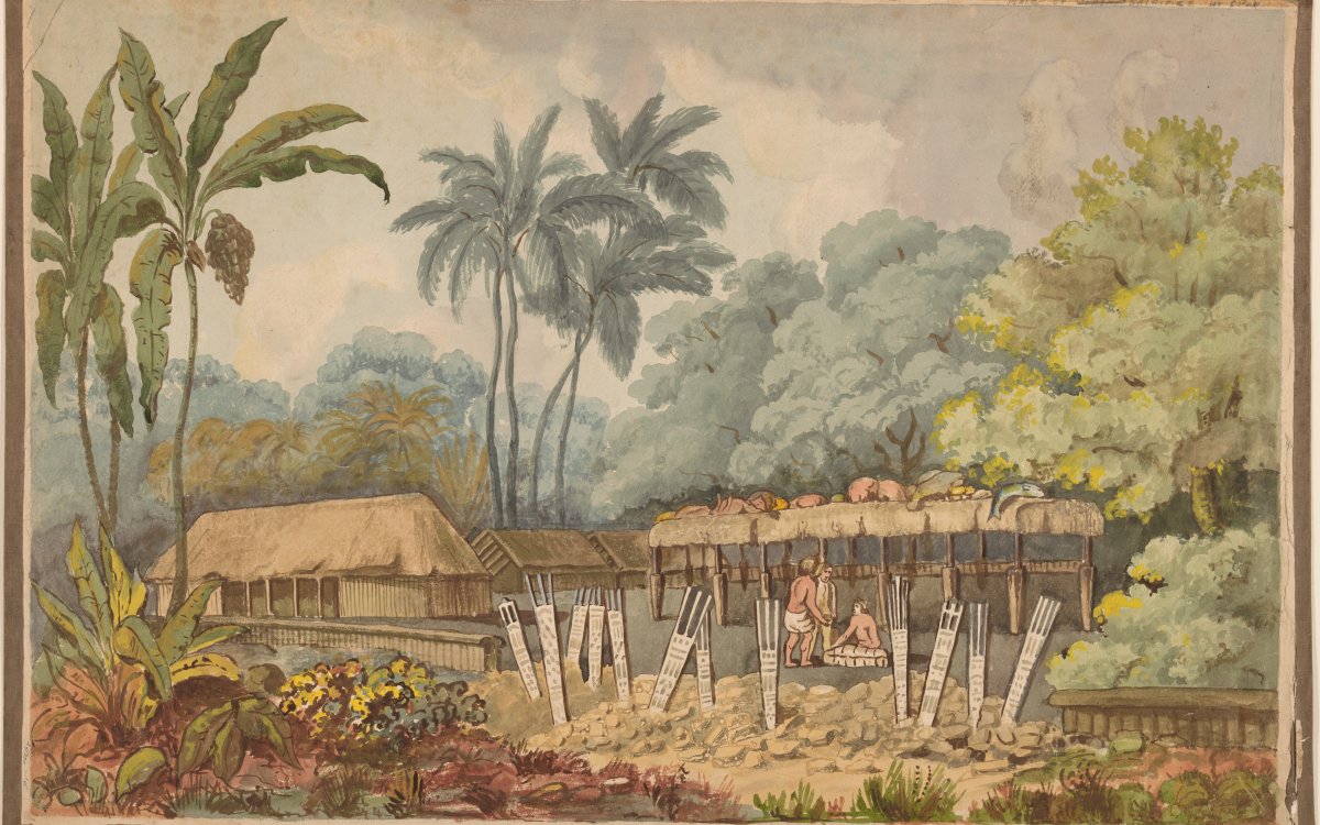 Two men are gathered under the shelter of a thatched roof structure. On top of the structure, offerings of meat and fish are strewn. In the foreground there are twelve signs or totems sticking out of the ground. To the left of the structure is a larger thatched roofed hut. The compound is surrounded by vegetation