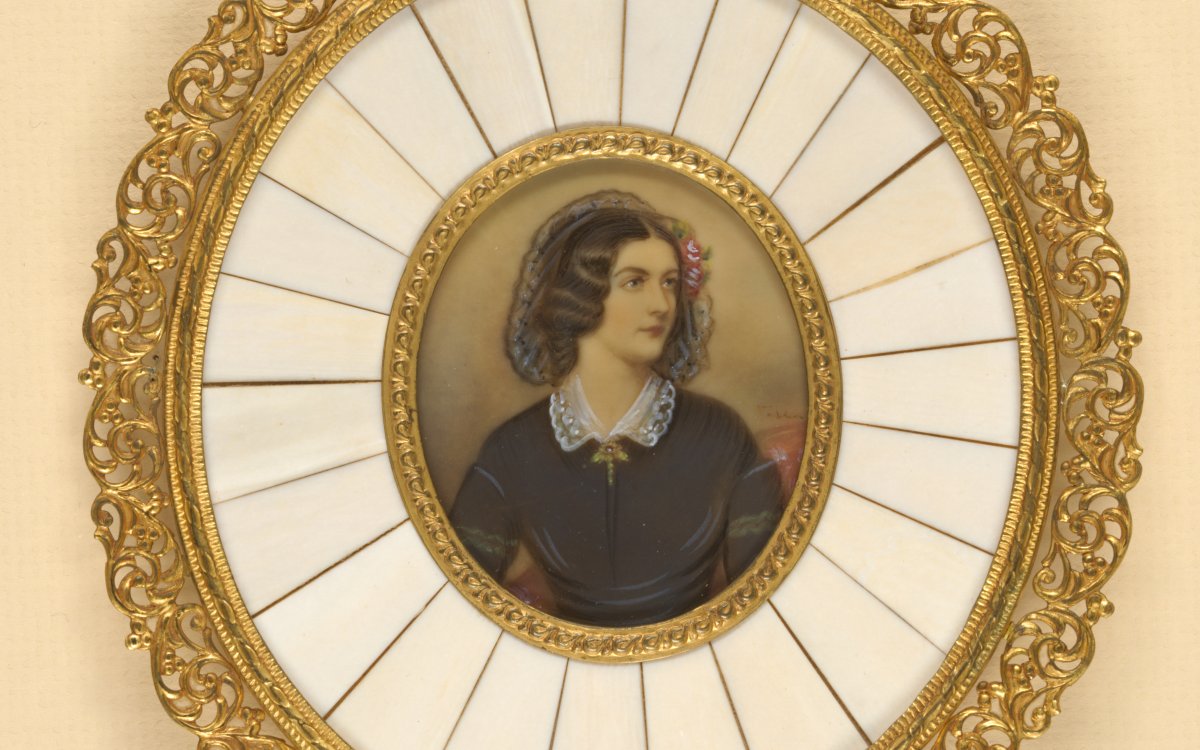 A round brooch with a gold filigree outer ring. White ivory inlay and a portrait of a lady dressed in a black dress.