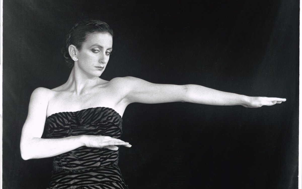 Ballerina Meryl Tankard strikes a pose. She is wearing a zebra print-esque dress. She is standing in front of a black curtain.