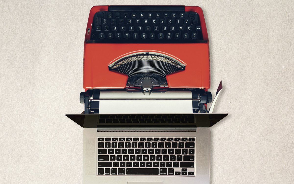 An image of a red typewriter back to back with an Apple laptop.