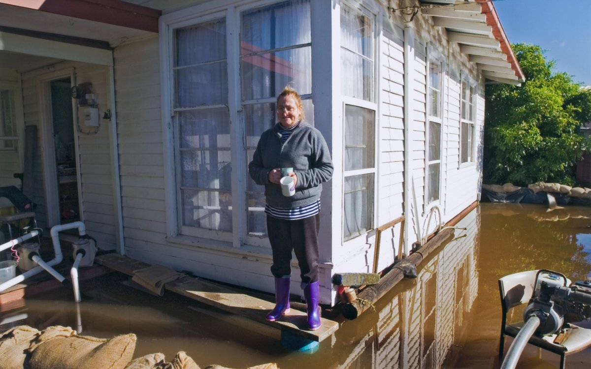 A person stands out side a house that is surrounded by sandbags. Water is up to the front step around the house.