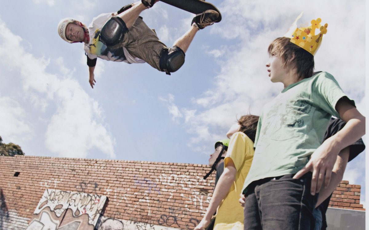 A man in the air doing a trick on a skateboard on the left with some young men watching him on the right