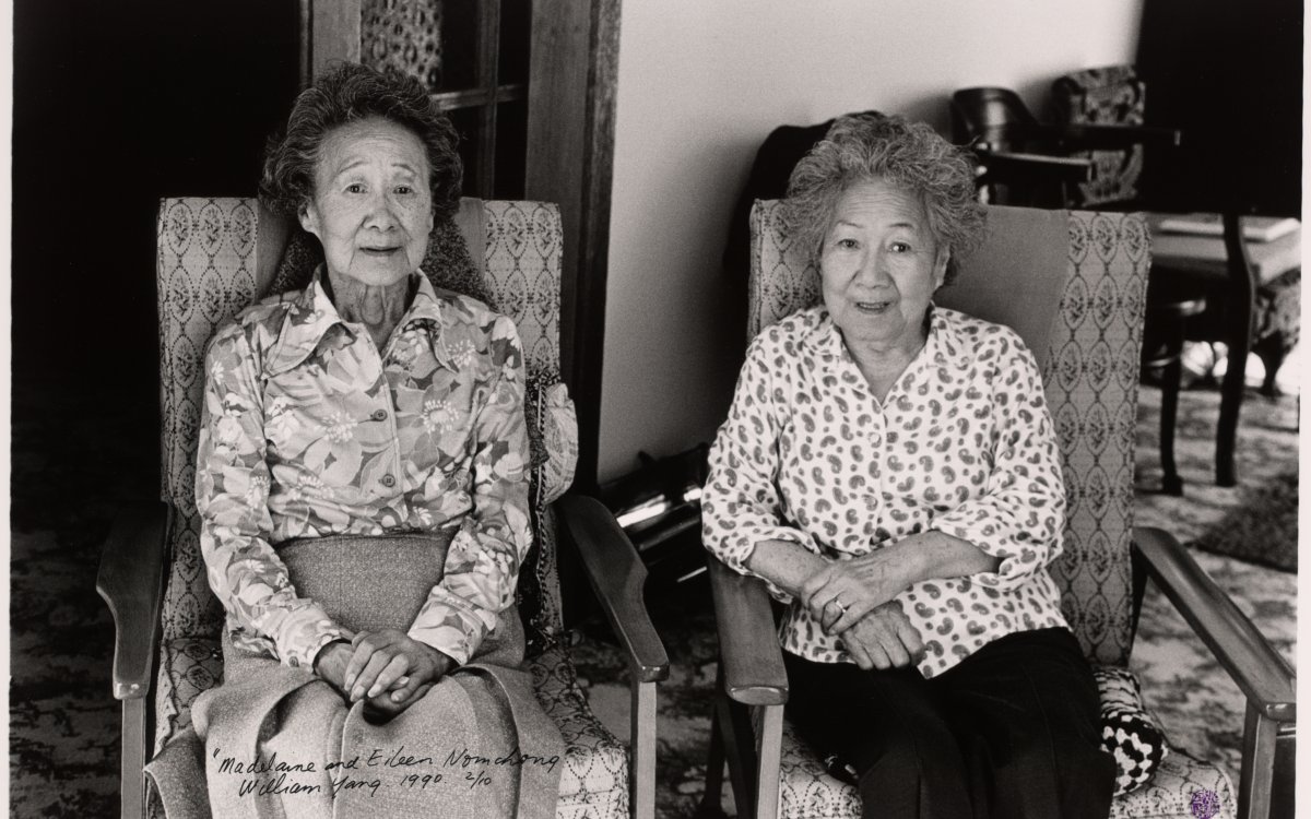 Two elderly women sitting in cushioned chairs looking at the camera with their hands folded in their laps.  