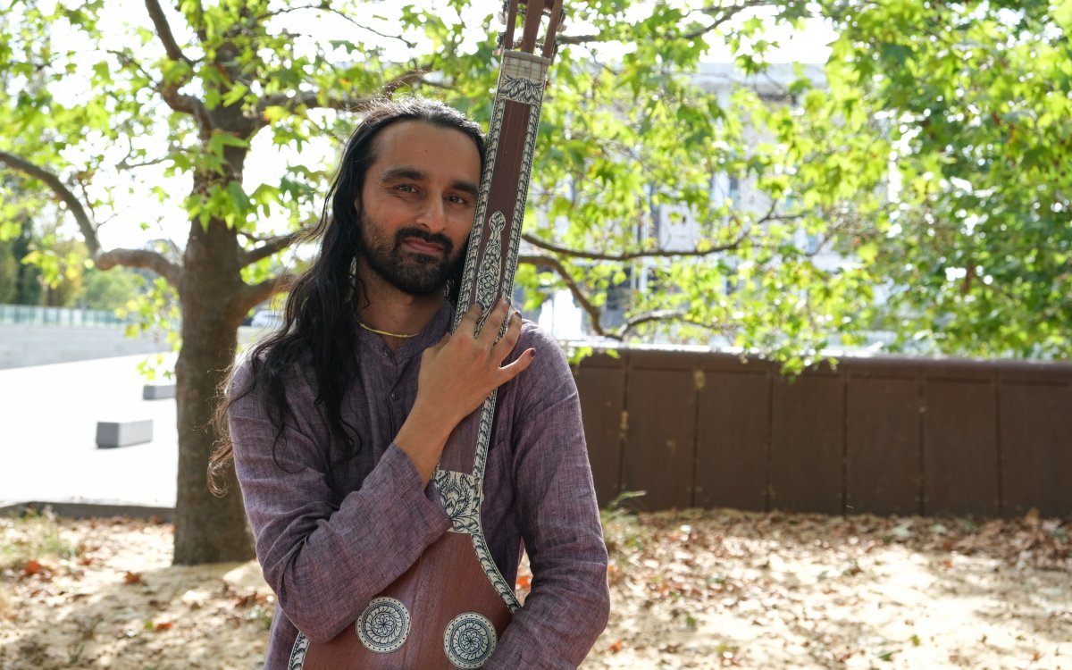 A person under a tree holding a stringed musical instrument.