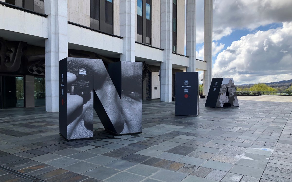 The front podium and colonnade of the Nationa Library of Australia, taken on an angle. On the podium are three huge letters; one 'N', one 'L' and one 'A'. The letters have blown up photographs on them.
