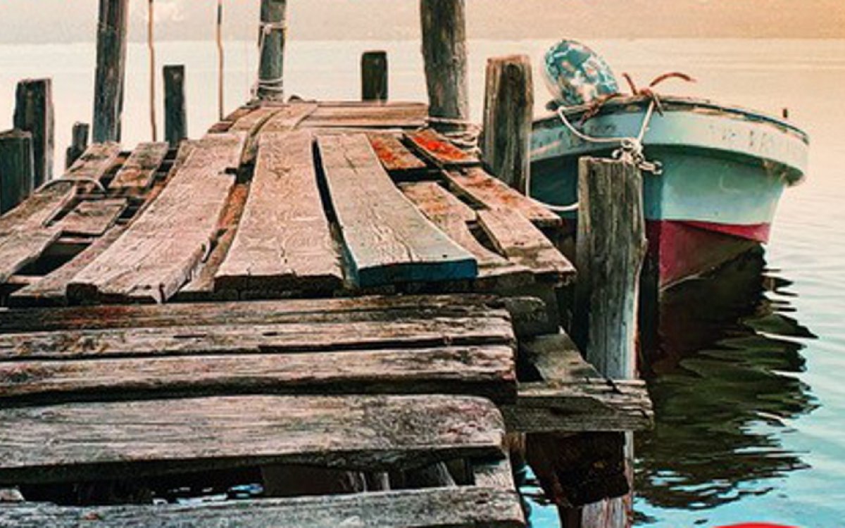 An image of an old, rickety jetty on the water, with a small boat ties up to it.