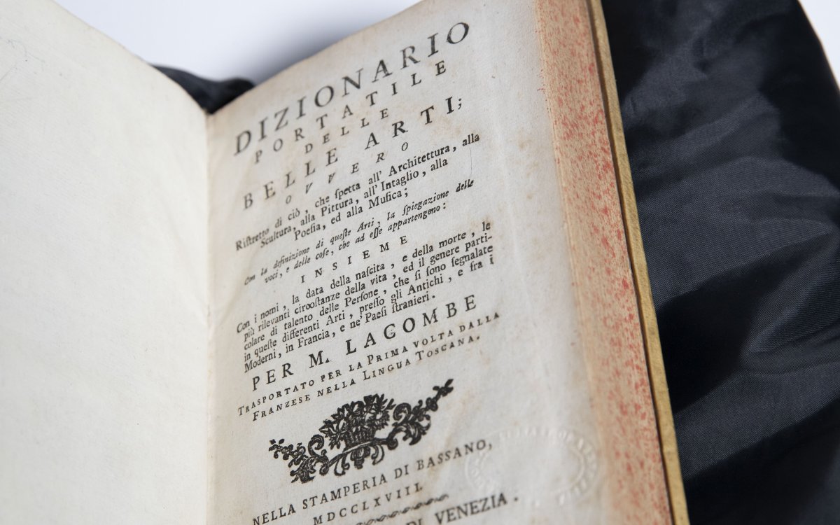 An old rare dictionary opened to a title page with lots of text titled 'Dizionario Portatile Delle Belle Arti'