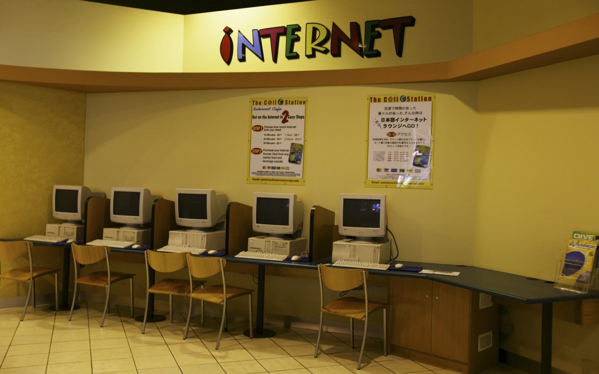A row of computers on a bench-desk. There is a big colourful sign saying INTERNET above them.