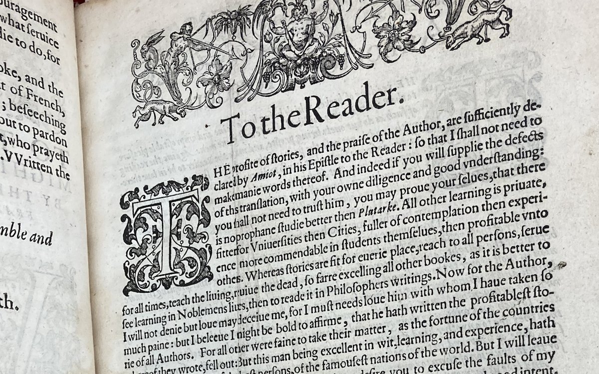 A book opened to a page of black text and visual embellishments. The heading on the page reads 'To the Reader'.