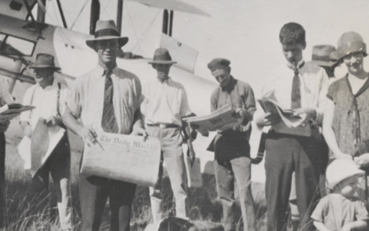 A group of men holding newspapers in front of airplane  