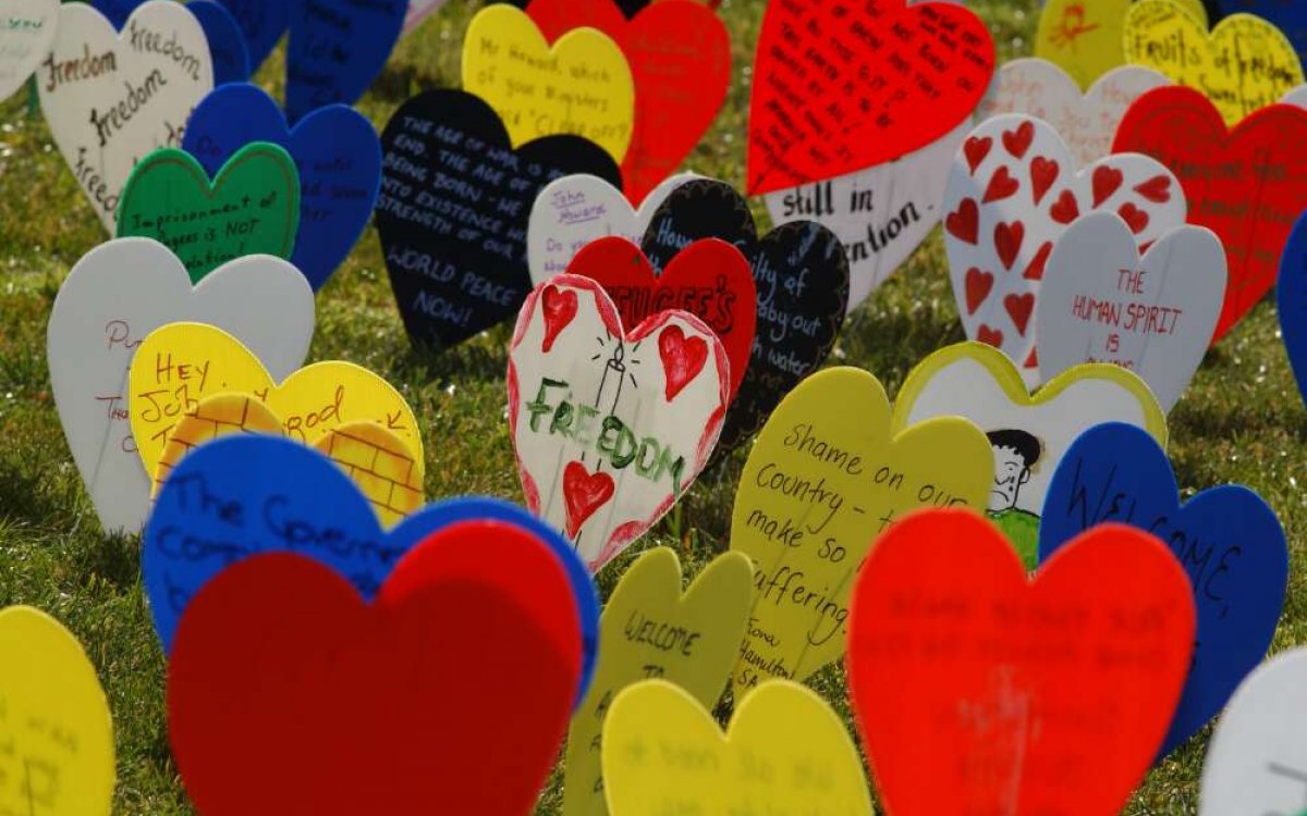 A photo of lots of different coloured plastic love hearts on a wire, stuck in a grassy area. The hearts are decorated with writing about freedom, and drawings.