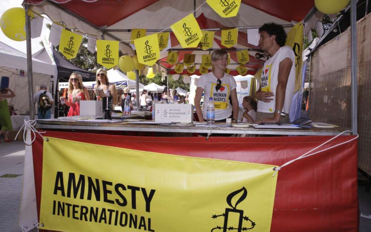 A photo of 2 people talking inside a market stall decorated with red and yellow signage reading 'Amnesty international'.