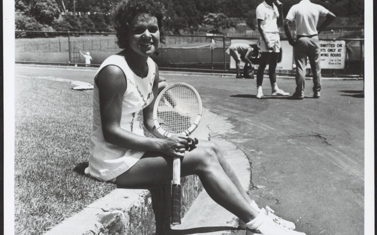 Black and white photo of Evonne Goolagong sitting holding a wooden tennis racket