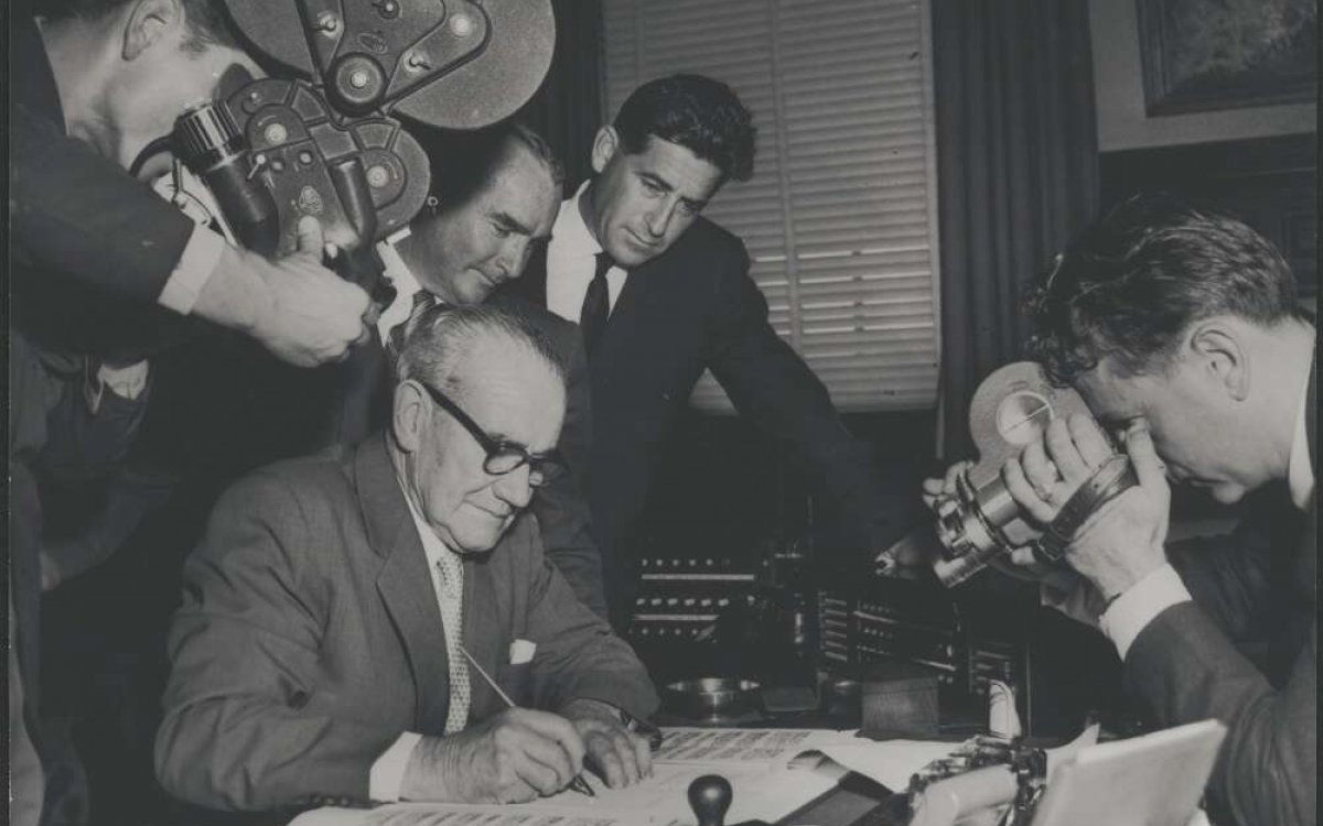 black and white photograph of man signing a contract being filmed