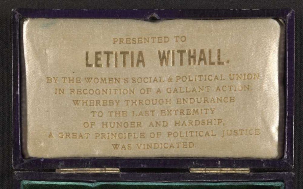 A medal with a green, white and purple ribbon. The medal is in a box with the words "Presented to Letitia Withall"