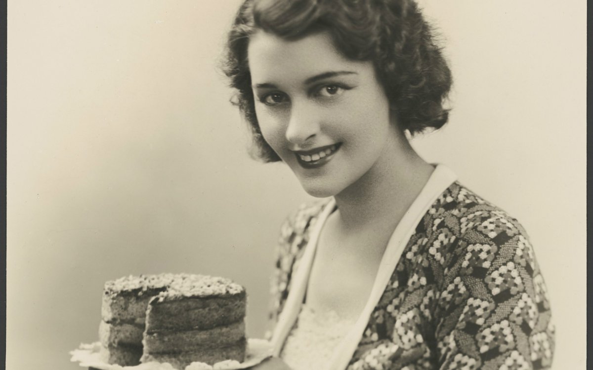 black and white photograph of a woman holding up a small cake with a slice taken out
