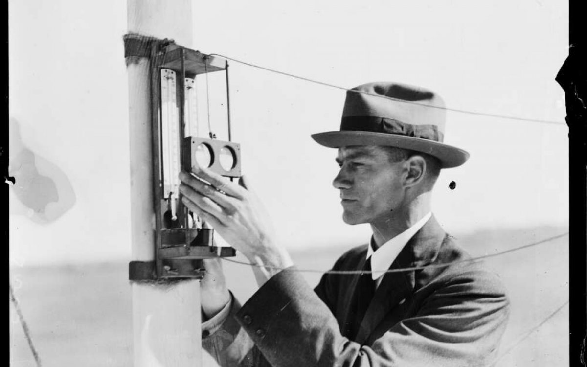 Black and white photo of a man in a hat reading thermometers