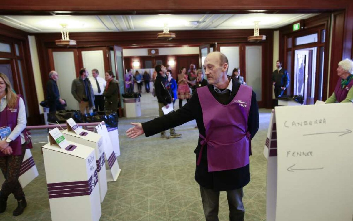 A photo of a man in a purple apron directing people toward ballot boxes.