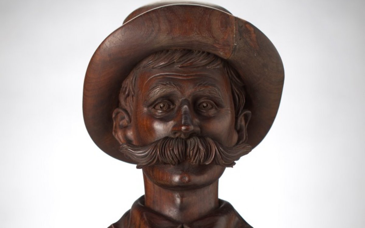 A wooden bust depicting the head and chest of Henry Lawson in a hat with large moustache.