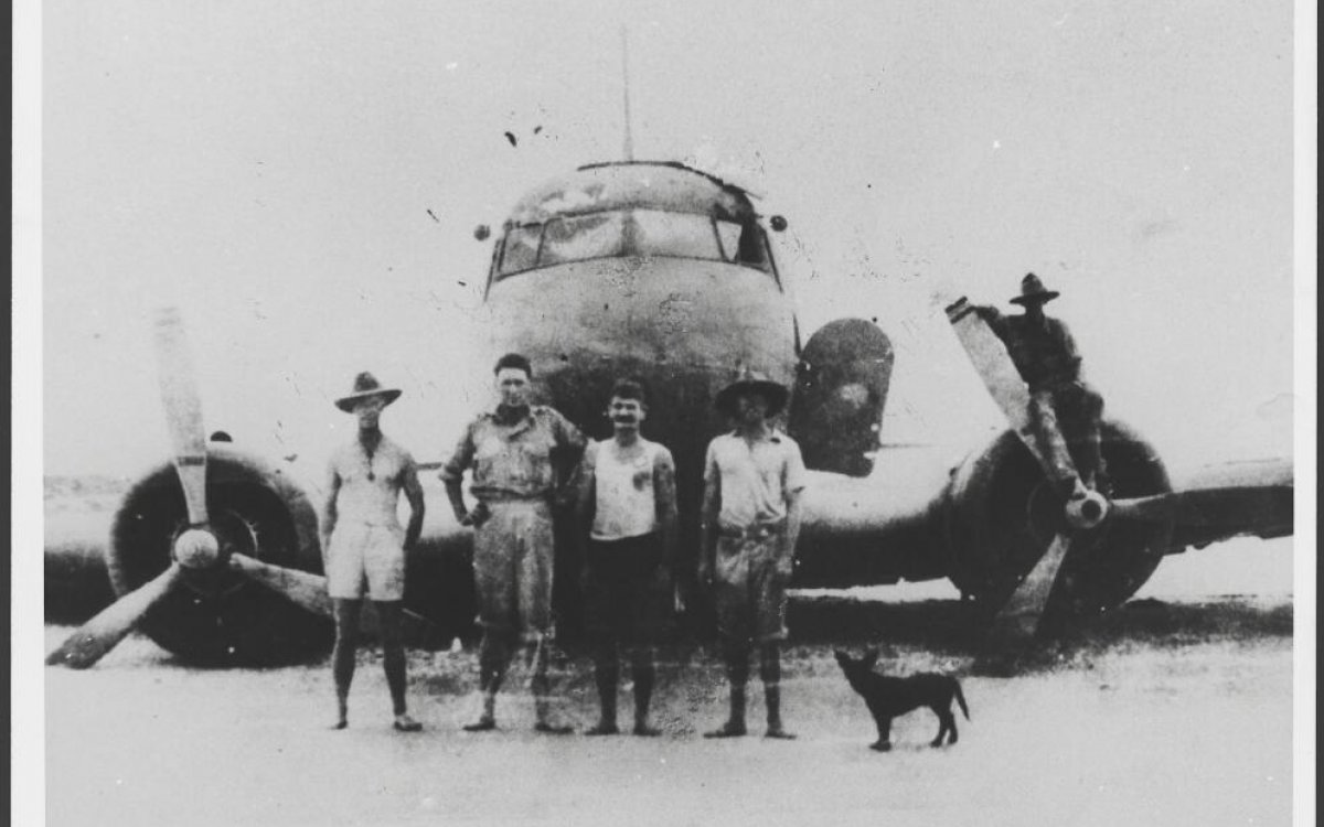black and white photograph of four men and a dog standing in front of a plane
