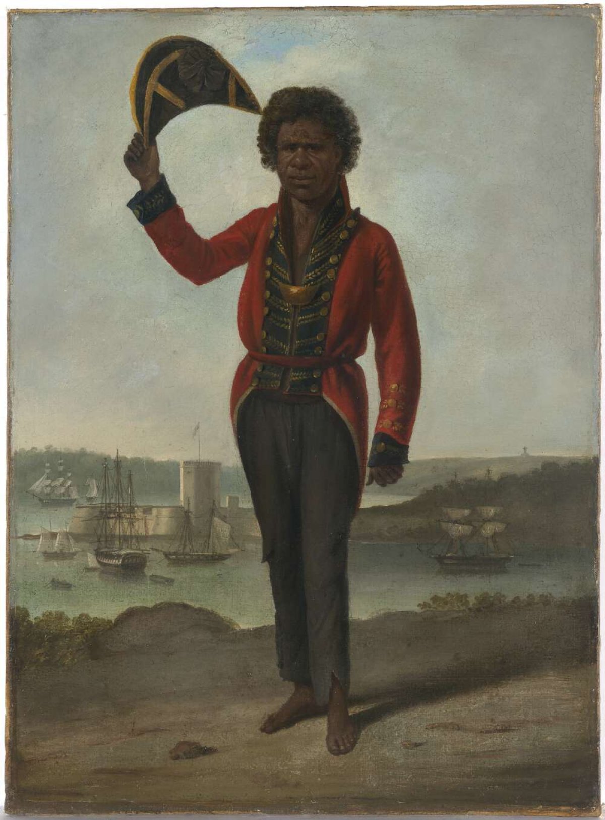 A portrait of a man. He has dark skin and hair. He is an Australian Indigenous man and is wearing a European style officers coat and trousers. His trousers are tattered at the cuffs. He is holding a tricorn hat in the air. In the background sailing ships can be see on the harbour. A large fort can be seen on a spit of land.