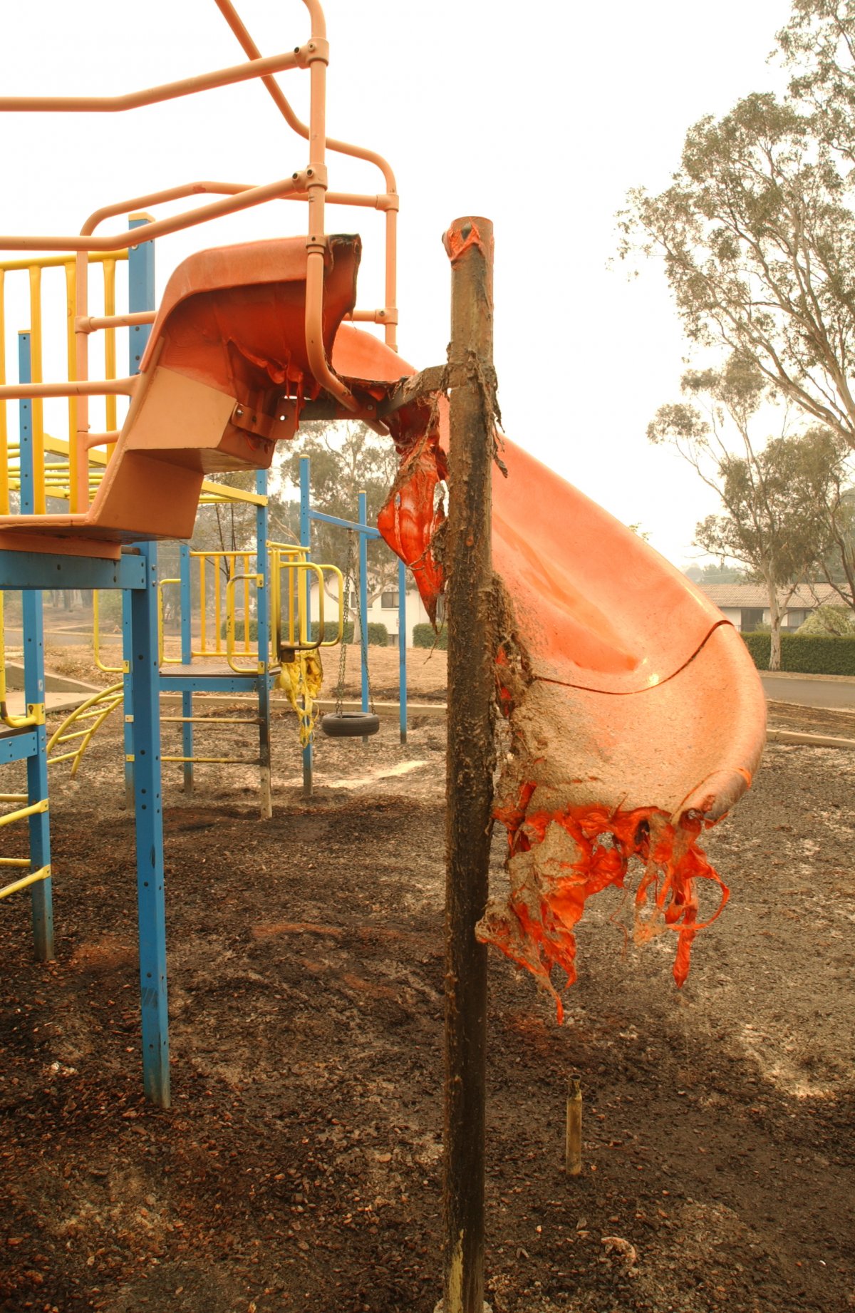 A children's playground slide is half melted after a fire burned through the playground. The surrounding metal of the playground is relatively untouched.