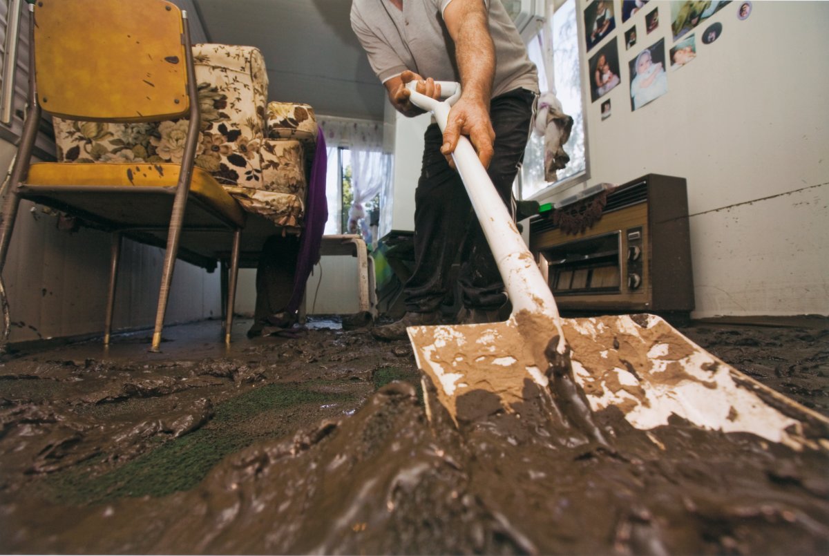 An interior shot of a room. A person is scooping up silt and mud with a shovel. The furniture is covered in mud.