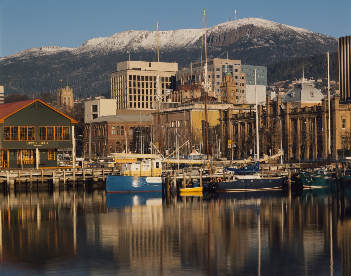 A city harbour scene. In the background a large snow capped mountain. There are several small boats on the water.