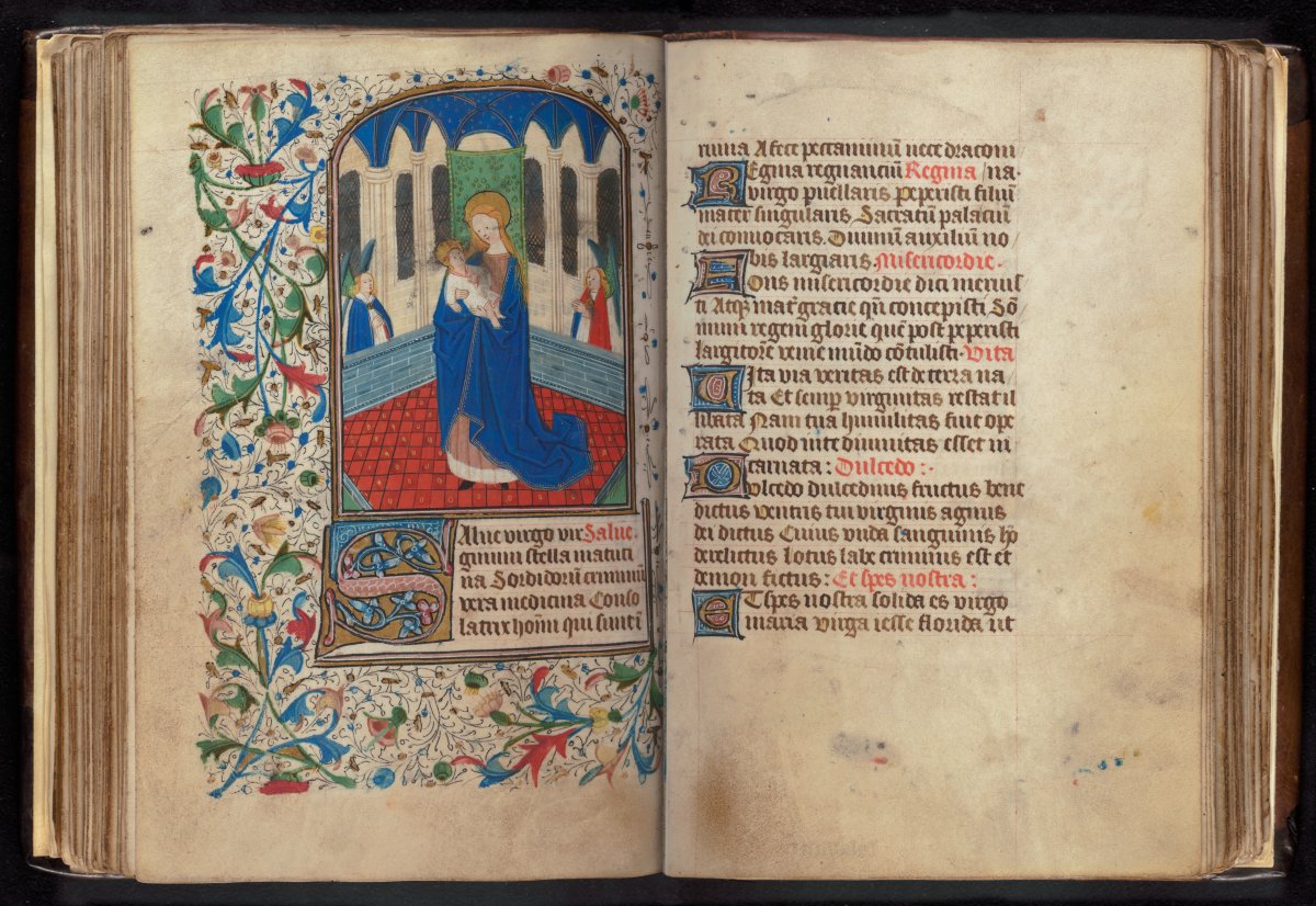 A composite image of a very old illuminated book. The left page is highly decorated and colourful. An image of a woman holding a baby is framed by plants. The right page is text written in black and red