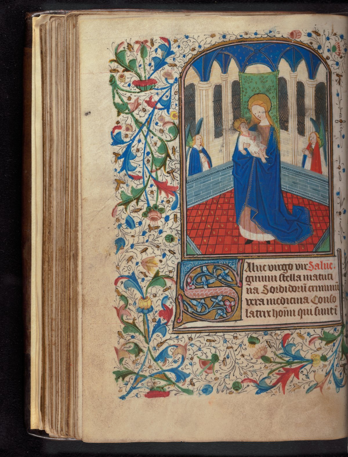 A handwritten page from a book of hours. The page is highly decorated and brightly coloured. An image of a woman holding a baby is framed by leaves and vines.