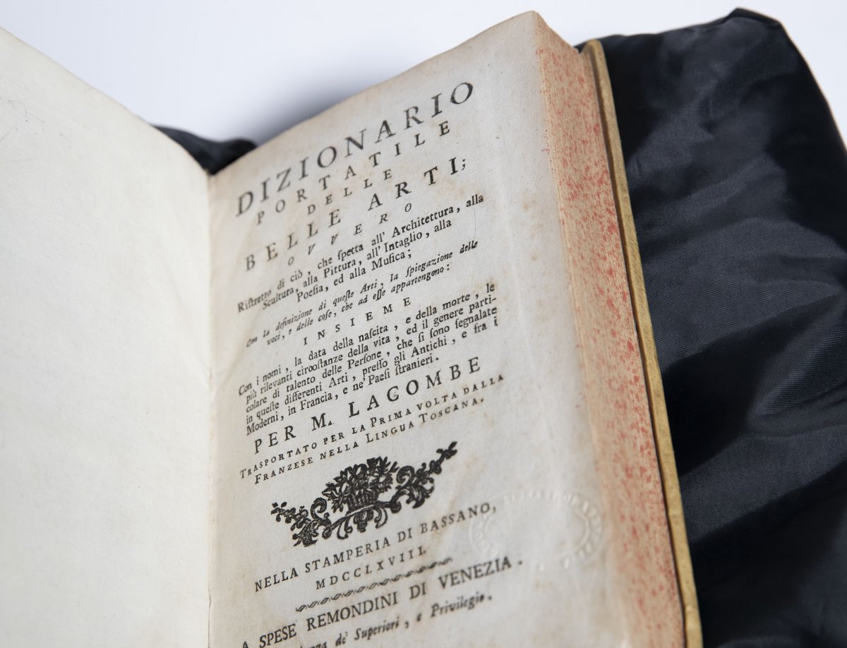 An old rare dictionary opened to a title page with lots of text titled 'Dizionario Portatile Delle Belle Arti'