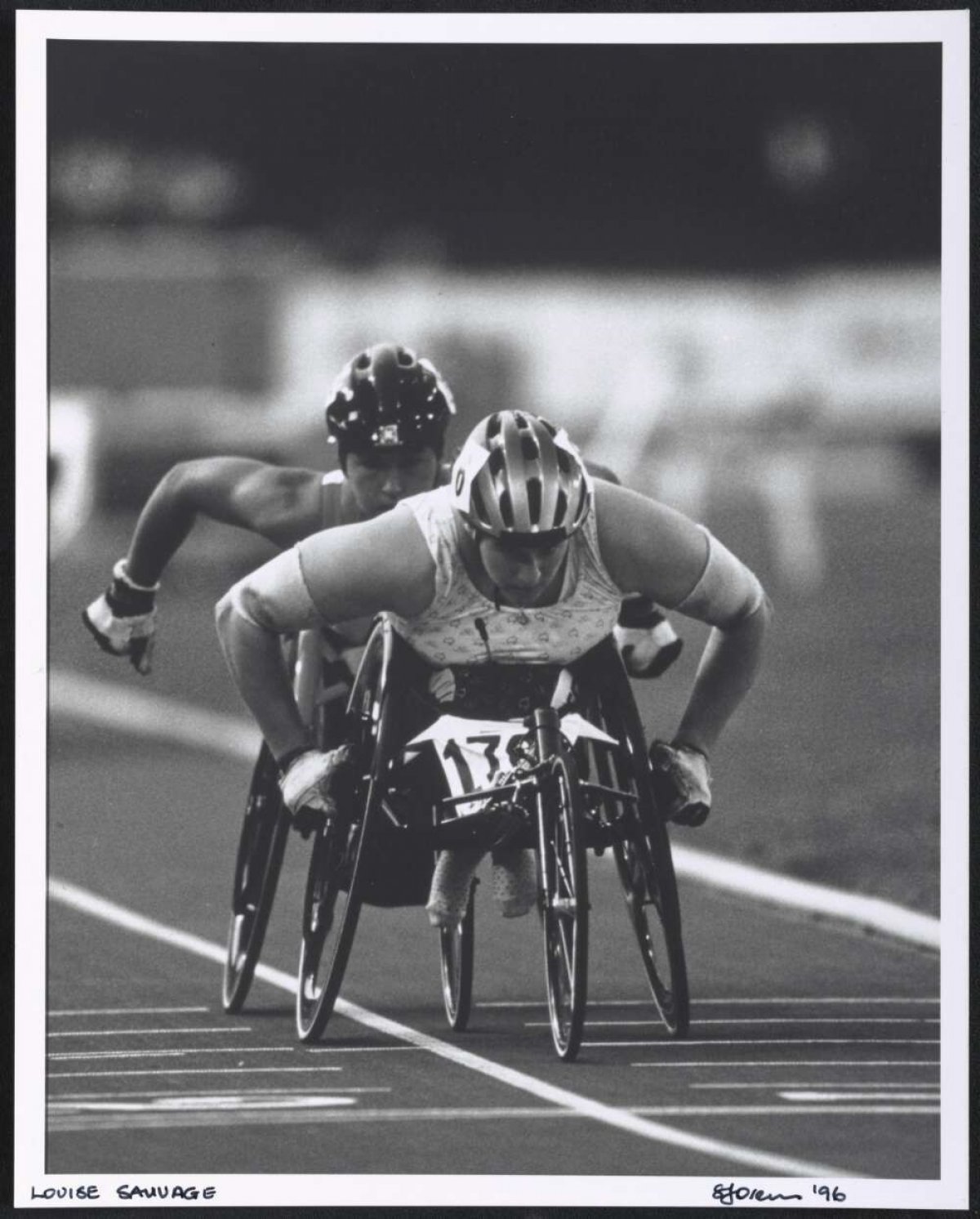 A black and white photo of Louise Sauvage leading another wheelchair racer on a track.
